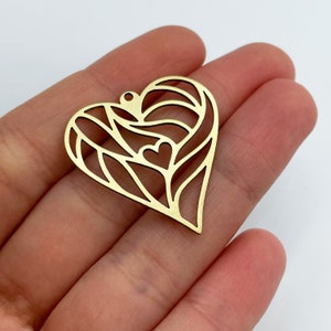 Op de afbeelding: Een gouden metalen hanger in de vorm van een hart met een delicaat, ingewikkeld ontwerp met kleinere harten binnen het grotere hart.