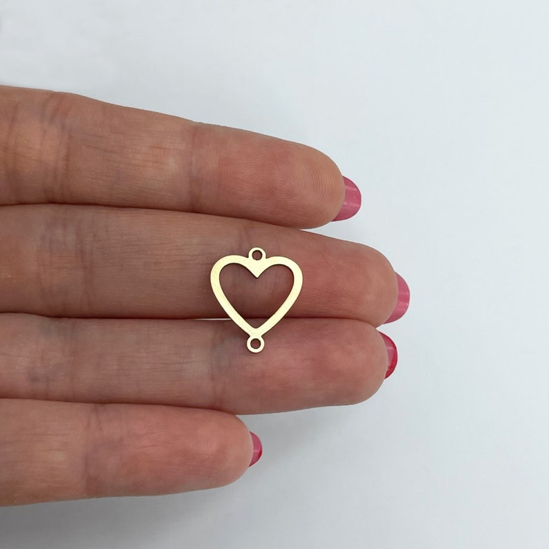 May include: Gold-toned metal heart charm with two jump rings. The heart is open and has a smooth finish.