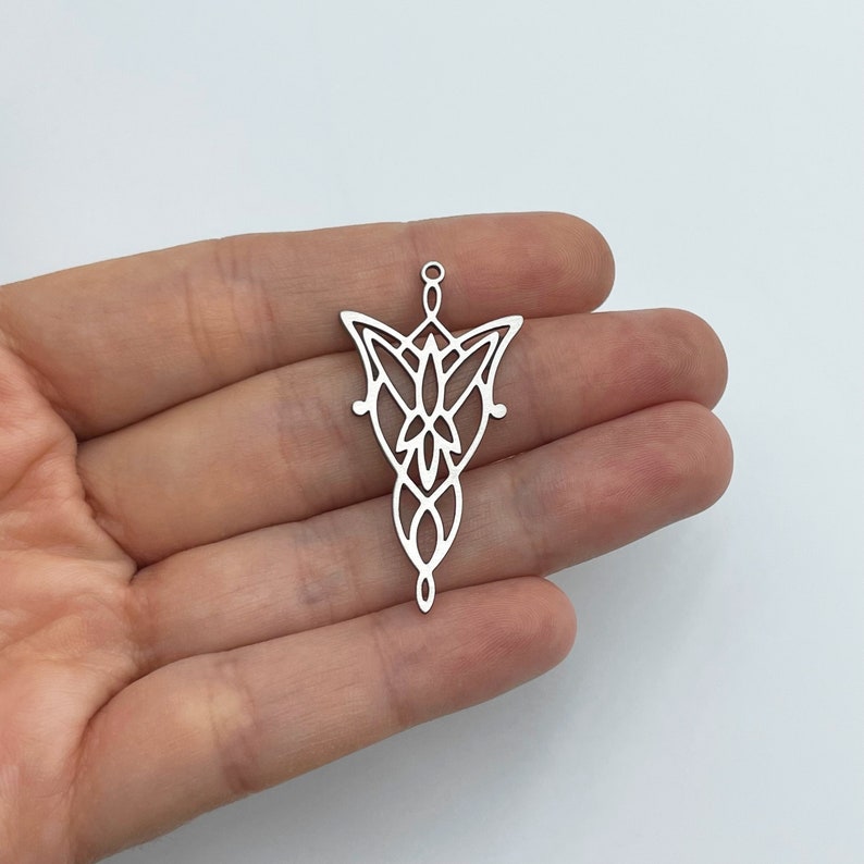 May include: Silver pendant featuring a detailed design of the One Ring symbol from The Lord of the Rings. The pendant is shown on a hand, showcasing its size and intricate details.