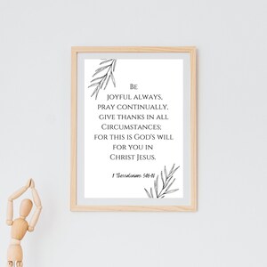 May include: A framed print with a light wood frame displays the text "Be joyful always, pray continually, give thanks in all circumstances; for this is God's will for you in Christ Jesus." Decorative leaf illustrations are at the top and bottom.