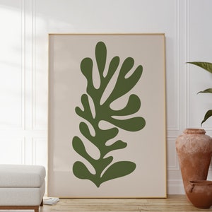 May include: A framed print of a stylised green leaf design on a beige background. The print is hanging on a white wall with a white ottoman in the foreground.