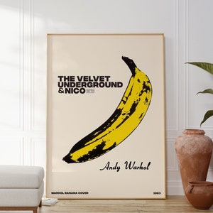 May include: A vintage poster featuring a yellow banana with black markings on a cream background. The text reads "The Velvet Underground & Nico with Andy Warhol" and "Warhol Banana Cover 1967".