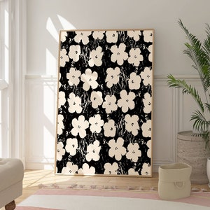 Könnte beinhalten: Ein gerahmter Schwarzweißdruck mit einem floralen Muster mit großen weißen Blüten auf schwarzem Hintergrund. Der Druck hängt an einer weißen Wand in einem Raum mit einem beigefarbenen Teppich und einer Topfpflanze.