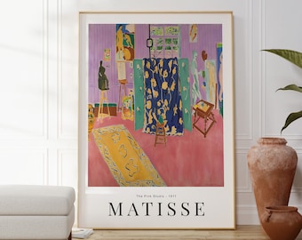 Könnte beinhalten: Ein gerahmter Druck von Henri Matisse' Gemälde "Das rosa Atelier", das eine farbenfrohe Innenszene mit einem rosafarbenen Boden, einem blau-gelb gemusterten Vorhang und mehreren Figuren zeigt. Der Druck ist mit "Das rosa Atelier - 1911" betitelt und unten mit "MATISSE" signiert.