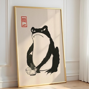 Può includere: Una stampa artistica incorniciata che raffigura un'illustrazione in bianco e nero di una rana imbronciata che tiene in mano una piccola ciotola. L'opera è su sfondo beige chiaro e include un timbro rettangolare rosso con i caratteri giapponesi 問一.