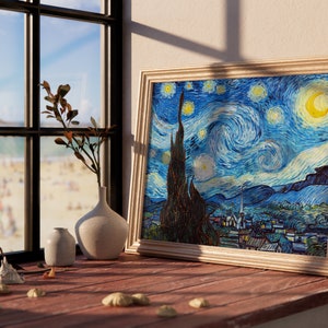 May include: A framed print of Vincent van Gogh's "Starry Night" painting, featuring a swirling blue sky with yellow stars and a crescent moon. The print is displayed on a wooden surface with a vase and a small plant.