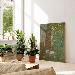 May include: A framed print of a colorful floral painting with sunflowers, red flowers, and green foliage. The print is hanging on a white wall in a room with houseplants and a wooden coffee table.