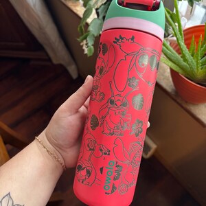 May include: A red Owala water bottle featuring a design of the character Stitch from Lilo & Stitch. The bottle has a green and pink lid. The bottle is covered in black line art of Stitch and tropical flowers.
