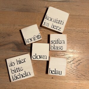 May include: Six small wooden signs with white backgrounds and black lettering. The signs read "konfetti im herz", "konfetti", "seifen blase", "clown", "ab hier bitte l&auml;cheln", and "helau".