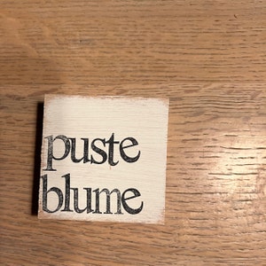 May include: A white wooden sign with black lettering that reads "puste blume".