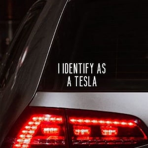 May include: A silver car with a rear window sticker that reads "I identify as a Tesla".