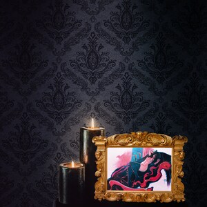 May include: A framed illustration of a woman in a red and black dress lying on a red and black patterned surface. The frame is gold and ornate. Two black candles are lit in front of the frame.