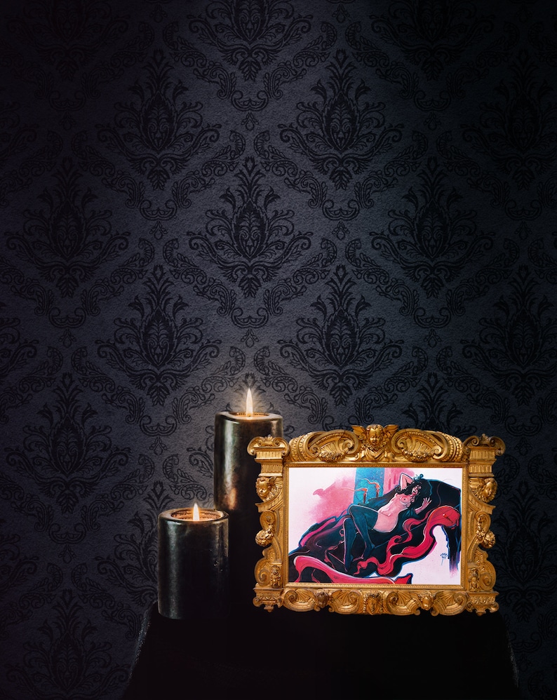 May include: A framed illustration of a woman in a red and black dress lying on a red and black patterned surface. The frame is gold and ornate. Two black candles are lit in front of the frame.
