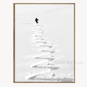 Pode incluir: Uma fotografia a preto e branco de um esquiador a fazer curvas em pó fresco numa montanha nevada. O esquiador está à distância, e a fotografia concentra-se nas marcas do esquiador na neve.