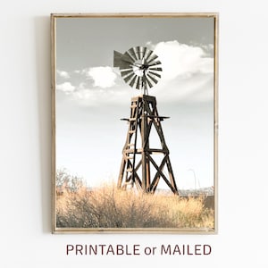 May include: A vintage wooden windmill with a weathered metal propeller stands tall against a cloudy sky. The windmill is surrounded by dry, golden grass.