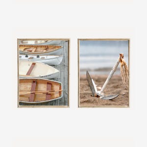 Könnte beinhalten: Ein Set aus zwei gerahmten Wandbildern. Das linke Bild zeigt vier hölzerne Ruderboote, die in einer Reihe an einem Holzsteg liegen. Das rechte Bild zeigt einen metallenen Bootsanker im Sand mit einem ausgefransten Seil am oberen Griff.