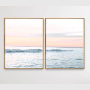 May include: A set of two framed prints featuring a seascape with a wave breaking in the foreground and a pink and blue sky in the background.