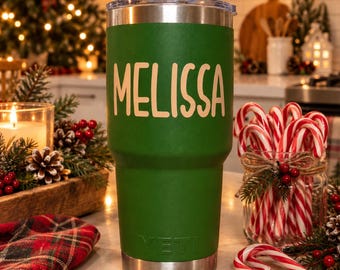 May include: A forest green stainless steel tumbler with a clear lid and a silver base. The name MELISSA is printed in large, light-colored capital letters on the front. The brand name YETI is embossed in a matching green tone near the bottom.
