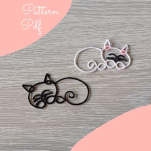 Può includere: Due figure di gatto di filo metallico, una nera e una bianca, sono esposte su una superficie di legno. Il gatto bianco ha accenti rosa sulle orecchie e sul naso, con dettagli neri per gli occhi e i baffi. Il testo "Pattern Pdf" è in alto a sinistra.