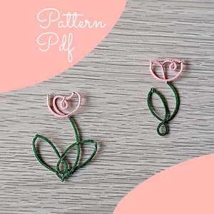 Puede incluir: Dos flores de tulipán de alambre con pétalos rosas y tallos y hojas verdes se muestran sobre una superficie de madera gris. El texto "Pattern Pdf" está escrito en cursiva en la esquina superior izquierda. El fondo tiene una superposición rosa.