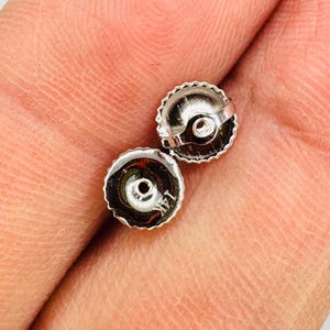 May include: Two small, silver-colored earring backs with a ridged edge and a central hole. The backs are marked with "14K". The image is a close-up, showing the details of the jewelry.