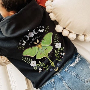 May include: Black hooded sweatshirt with a green luna moth graphic and the text "You are magic" on the back. The moth is surrounded by white flowers and stars.