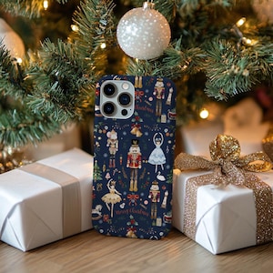 May include: A navy blue phone case featuring a festive Christmas design. The case showcases illustrations of nutcrackers, ballerinas, and Christmas trees. The words "Merry Christmas" are also visible on the case. The case is surrounded by wrapped gifts and Christmas tree ornaments.