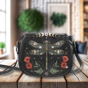 May include: Black leather crossbody bag with a dragonfly design, red poppies, and gold accents. The bag has a long adjustable strap.