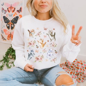 May include: White sweatshirt with a colorful print of kittens playing with butterflies and flowers.