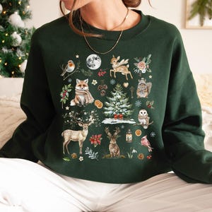 May include: A dark green sweatshirt with a festive winter scene printed on the front. The design features a variety of animals, including a fox, deer, and a bird, along with a Christmas tree and other wintery elements.