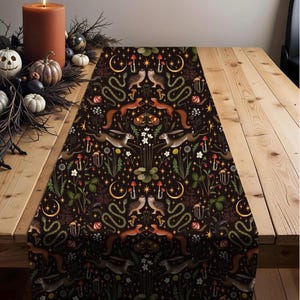 Pode incluir: Caminho de mesa castanho escuro com um padrão repetido de criaturas da floresta, incluindo esquilos, corujas, cobras e coelhos. O design também apresenta cogumelos, luas crescentes e estrelas. O caminho de mesa está colocado sobre uma mesa de madeira.