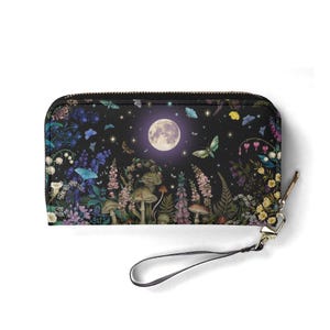 May include: Black zip-around wallet with a whimsical nighttime forest scene. The design features a full moon, butterflies, mushrooms, and various flowers in shades of purple, blue, and green. Includes a wrist strap and gold-tone zipper.
