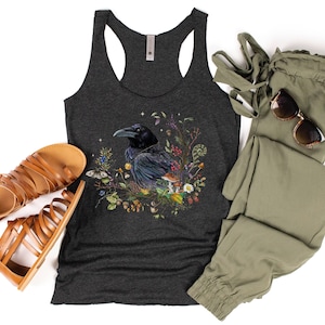 K&ouml;nnte beinhalten: Ein dunkelgraues Tanktop mit einem schwarzen Raben, umgeben von bunten Blumen und Pilzen. Das Tanktop hat einen Racerback-Stil.