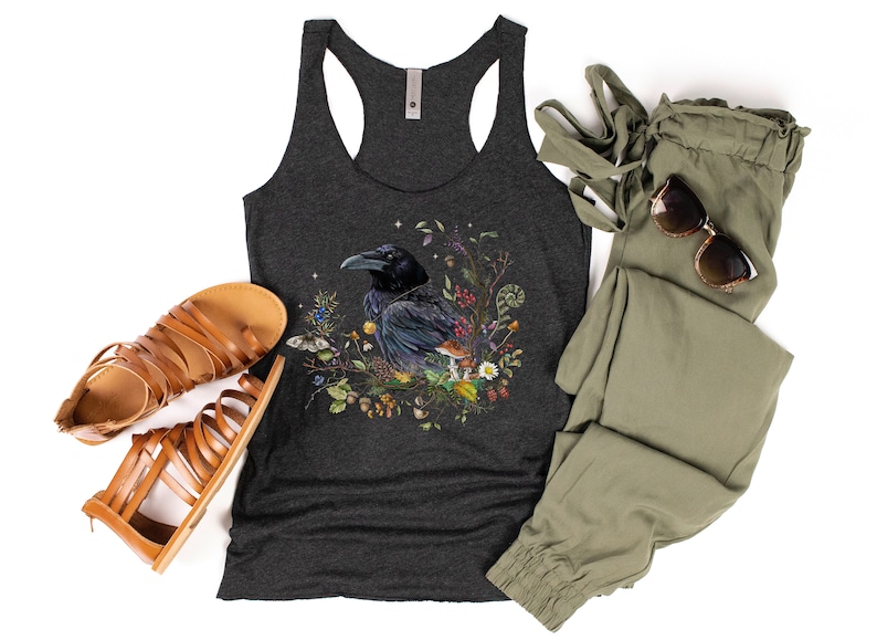 K&ouml;nnte beinhalten: Ein dunkelgraues Tanktop mit einem schwarzen Raben, umgeben von bunten Blumen und Pilzen. Das Tanktop hat einen Racerback-Stil.