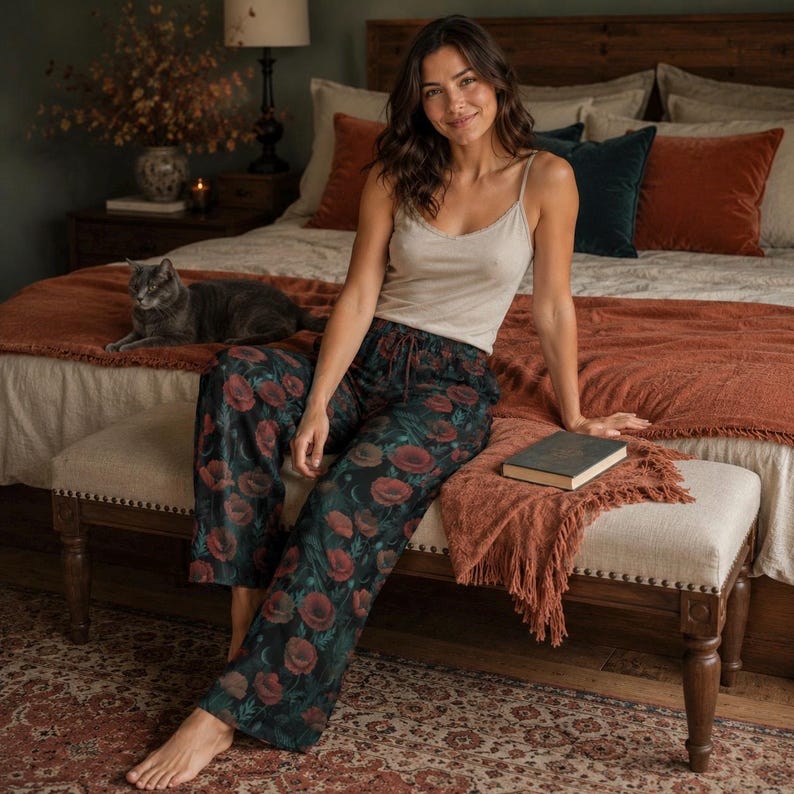 May include: A beige camisole with a delicate lace trim neckline paired with loose-fitting dark green pajama pants featuring a vibrant red poppy flower print and a drawstring waist. The pants have a wide-leg silhouette and a repeating floral pattern.