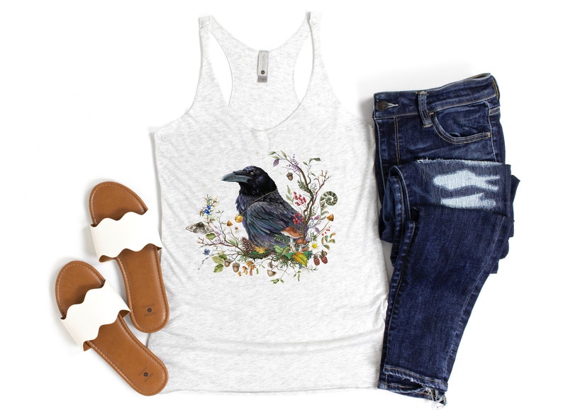K&ouml;nnte beinhalten: Ein wei&szlig;es Tanktop mit einer schwarzen Rabenillustration, umgeben von Blumen, Bl&auml;ttern und Beeren. Der Rabe sitzt auf einem Ast und hat ein detailliertes Design. Das Tanktop ist in der Farbe Grau meliert und hat einen Racerback-Stil.
