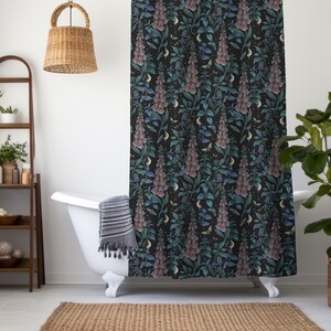 May include: A black shower curtain with a floral pattern featuring pink and blue flowers, green leaves, and crescent moons. The shower curtain is hanging in a bathroom with a white bathtub and a wooden ladder shelf.