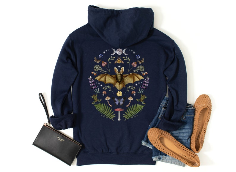 May include: Navy blue hooded sweatshirt featuring a graphic print of a bat surrounded by flowers, mushrooms, and other woodland elements. The graphic is in a circle with a crescent moon and stars above the bat.