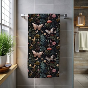 Peut inclure: Une serviette de bain noire avec un motif floral et papillon. Le motif présente des papillons roses, blancs et verts sur un fond foncé avec des feuilles vertes et des fleurs roses.