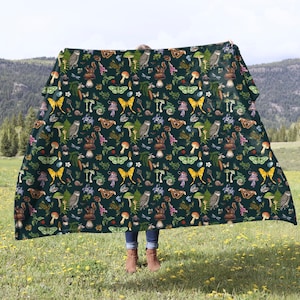 May include: A dark green throw blanket with a repeating pattern of mushrooms, butterflies, owls, and other forest creatures.