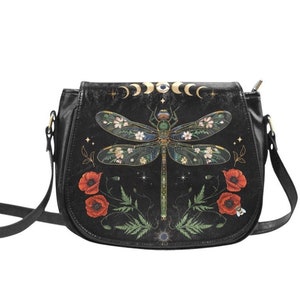 May include: Black leather crossbody bag with a dragonfly design. The dragonfly is surrounded by flowers and stars. The bag has a gold chain strap.