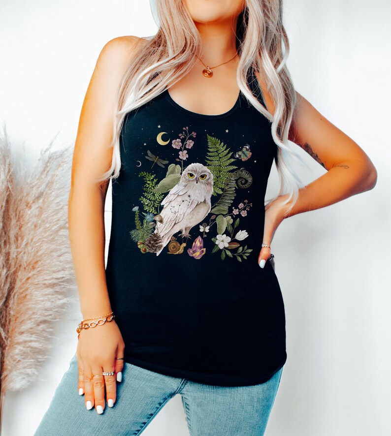 May include: Black vest top with a detailed illustration of a white owl surrounded by botanical elements. The design includes ferns, flowers, a crescent moon, and a dragonfly. The owl has yellow eyes and is perched among the foliage.