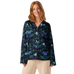 May include: A button-down shirt with a dark background, featuring a pattern of blue butterflies, thistles, and floral elements in shades of teal and purple. The long-sleeved shirt has a classic collar and is worn with beige pants.