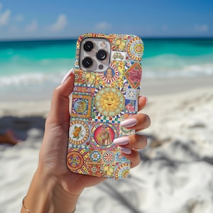 May include: A colorful phone case featuring a mosaic design with a sun, flowers, and other decorative elements. The case has a glossy finish and a multi-colored pattern. The phone case is held in front of a beach background.