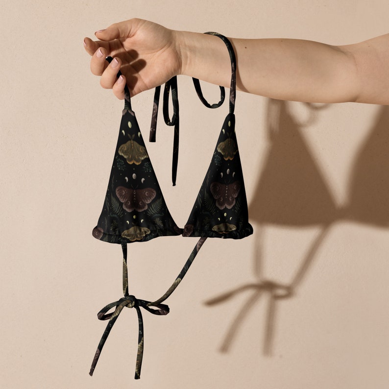May include: A black triangle bikini top with a floral and butterfly print. The top has adjustable straps and ties at the back.