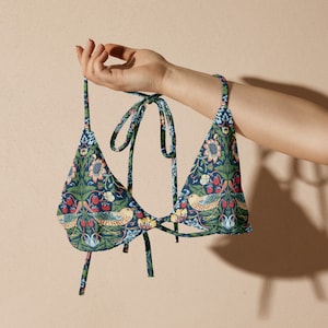 May include: A blue and green patterned bikini top with a floral and bird design. The top has adjustable straps and a tie closure at the back.