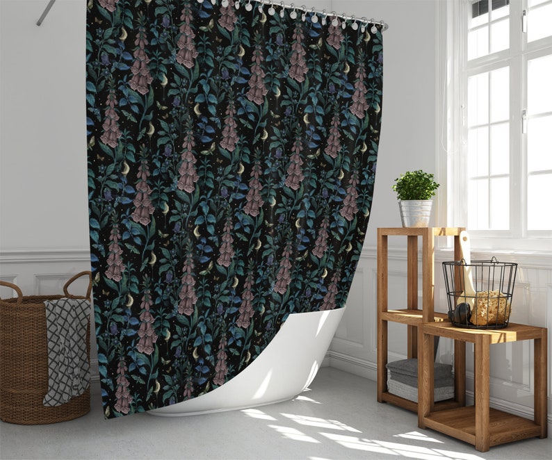 May include: A black shower curtain with a floral pattern featuring pink and blue flowers on a dark background. The flowers are stylized and resemble foxgloves. The curtain is hanging in a bathroom with a white bathtub and a wooden shelf unit.