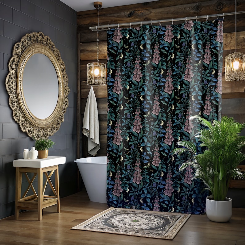 May include: A black shower curtain with a floral pattern featuring pink and blue flowers, green leaves, and gold crescent moons. The shower curtain is hanging in a bathroom with a white bathtub, a wooden floor, and a gold mirror.