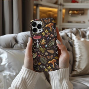 May include: A black phone case with a colorful mushroom, butterfly, and leaf pattern. The case has a camera lens cutout and a white border.