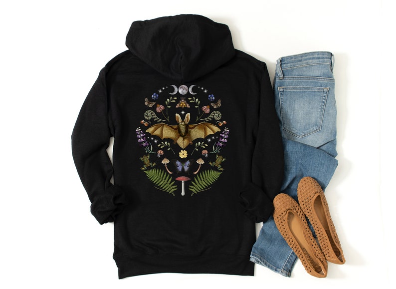 May include: Black hooded sweatshirt featuring a graphic print of a bat surrounded by flowers, mushrooms, and other woodland elements. The graphic is in shades of brown, green, purple, and yellow.